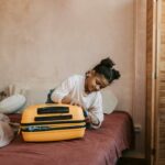 A young girl packs a bright yellow suitcase on a bed, preparing for travel.